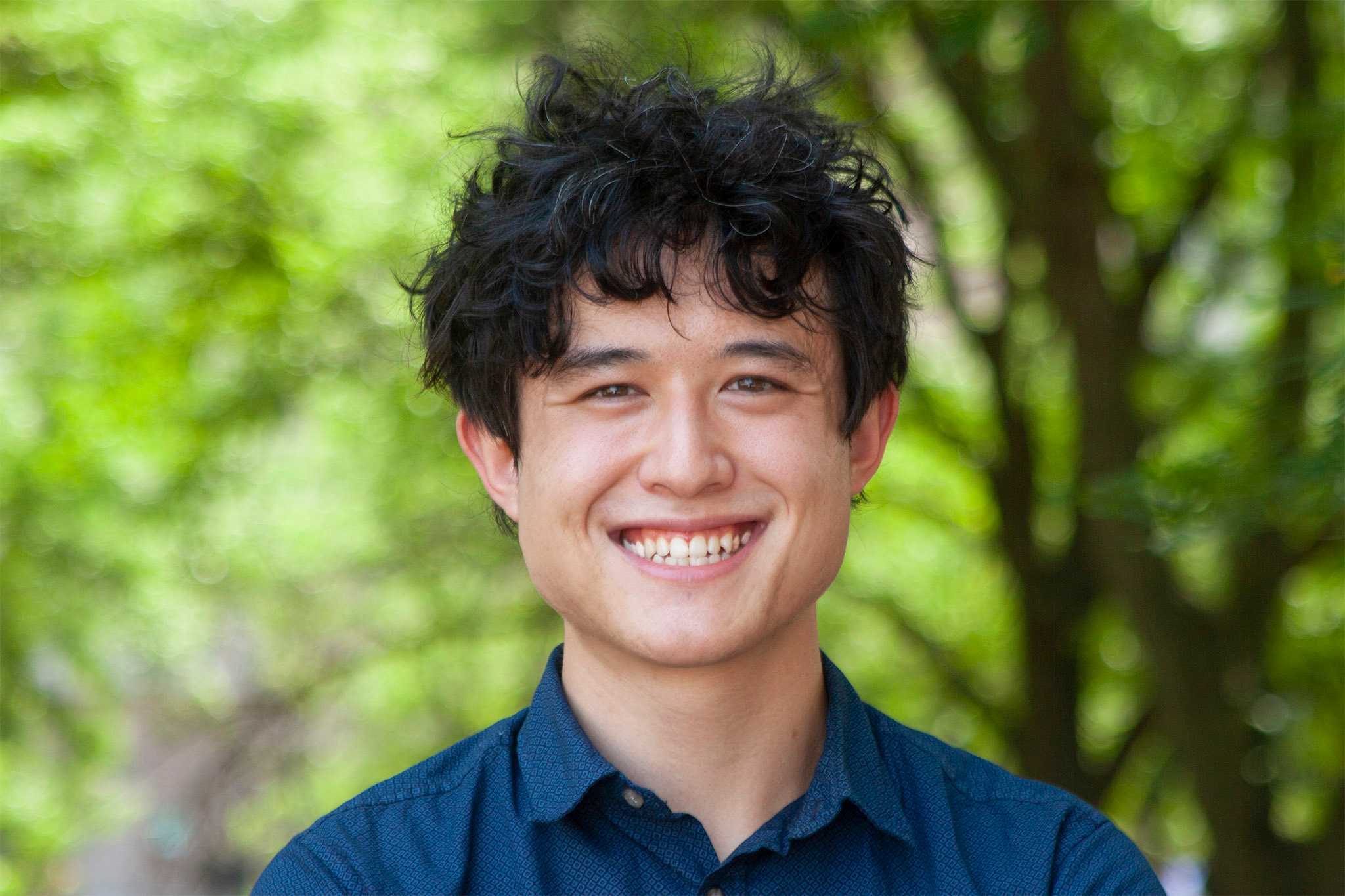 A portrait of Ben Pettis. He is framed from the shoulders up, and is wearing a blue shirt and standing in front of a semi-blurry green background.